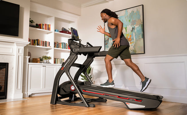 Side view of a man running on a BowFlex Treadmill T10 in a bright living room.