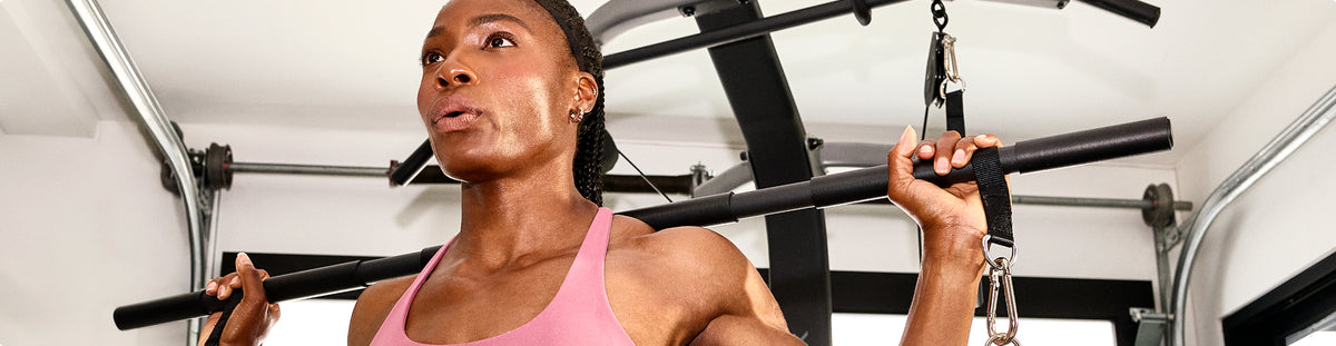 A woman in a pink sports tank top using the 6-grip steel straight bar attachment on the BowFlex Xtreme 2 SE Home Gym.