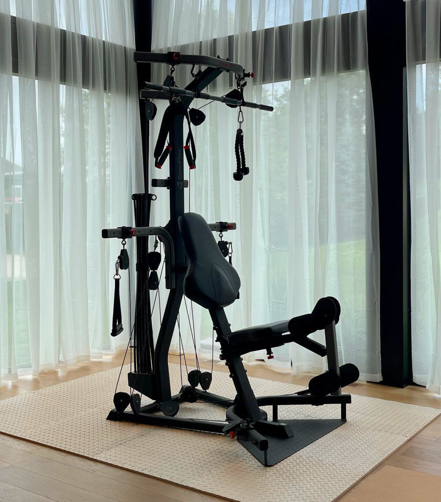 The BowFlex Xtreme 2 SE Home Gym set on a textured beige mat in a room with sheer white curtains.