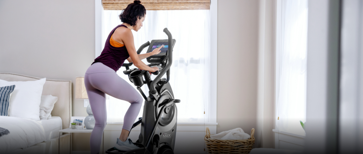 A woman working out on a Max Trainer compact elliptical in her bedroom.